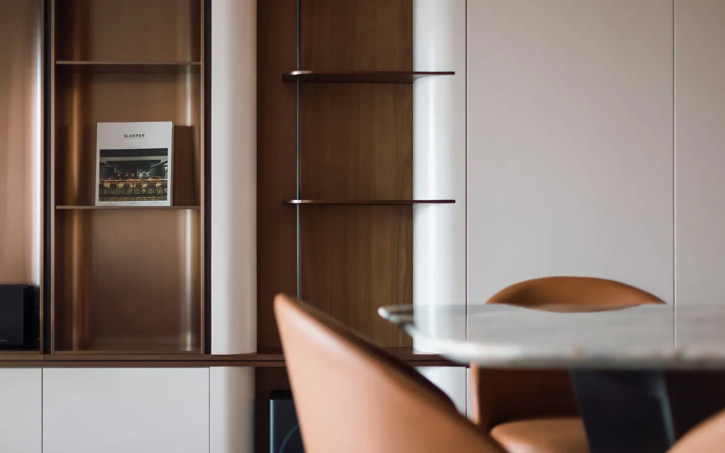 Elegant dining space designed by Rebel Arkitekt, featuring an italian stone dining table, tan leather chairs, and a bespoke shelving unit with a minimalist decor book, exemplifying luxurious yet understated residential design.