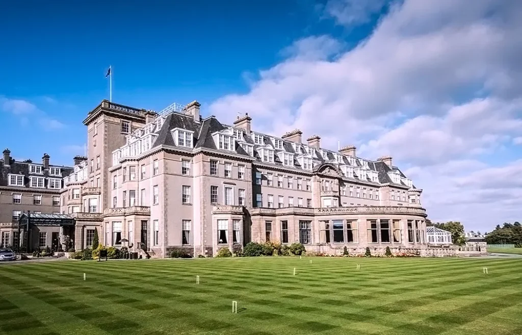 Historic Gleneagles Hotel with landscaped lawn under a clear blue sky.