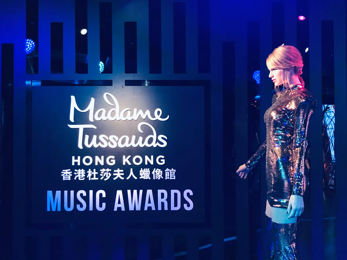 A wax figure dressed in a sparkling outfit at Madame Tussauds Hong Kong, with a sign for "Music Awards" illuminated in blue and white lights.