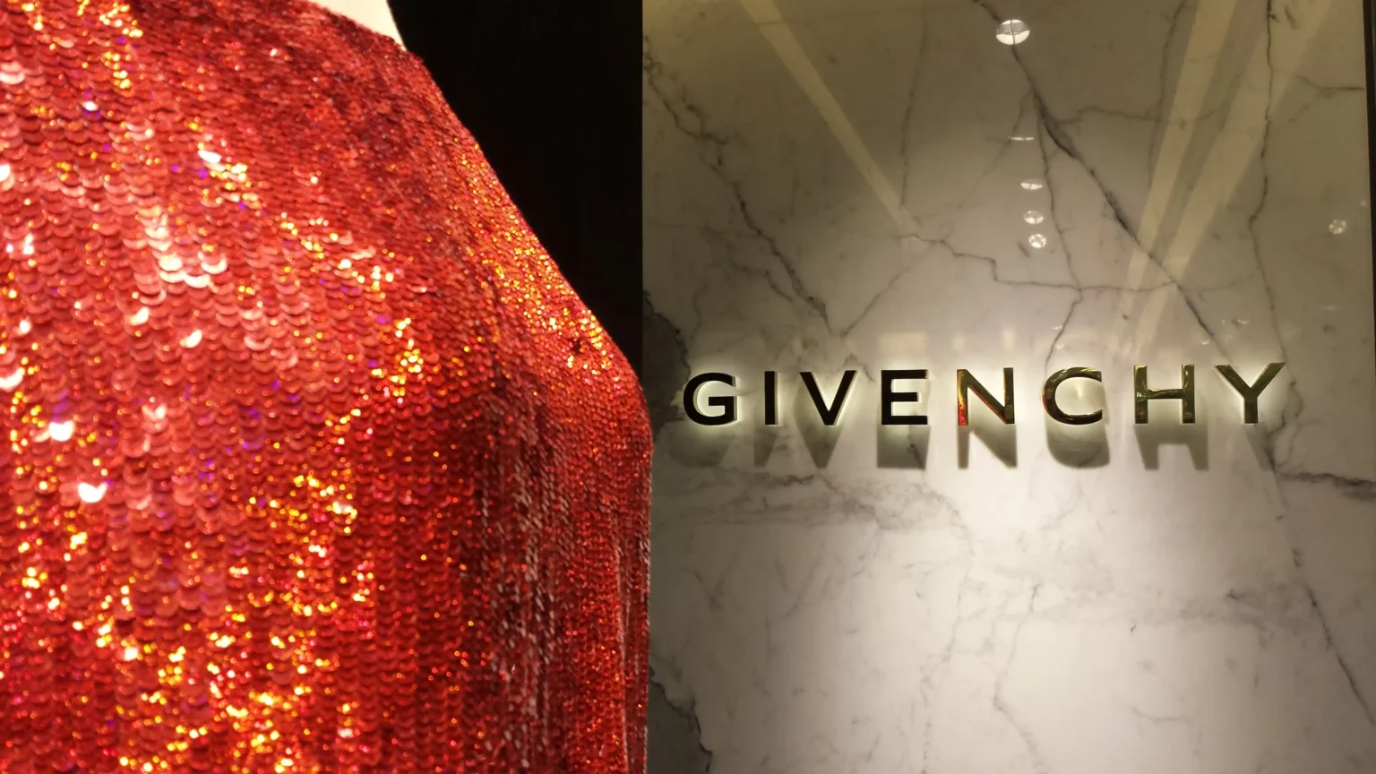 Close-up of a glittering red sequined garment with the word "GIVENCHY" on a white marble background.