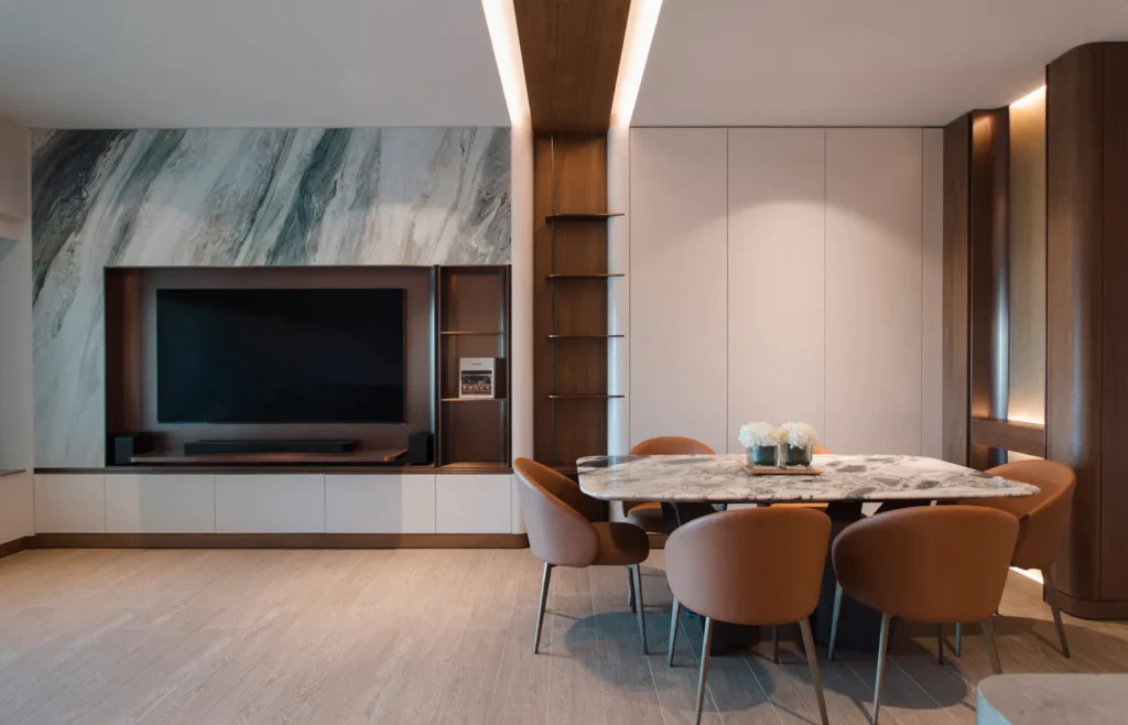 A refined living room corner by Rebel Arkitekt with stone wall detailing, custom cabinetry, and a modern dining setup, bathed in soft ambient lighting that accentuates the luxurious finishes.