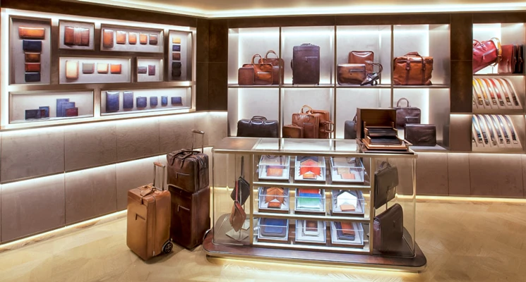 Elegant display of leather goods with wallets, handbags, and suitcases under soft lighting in a luxury store.