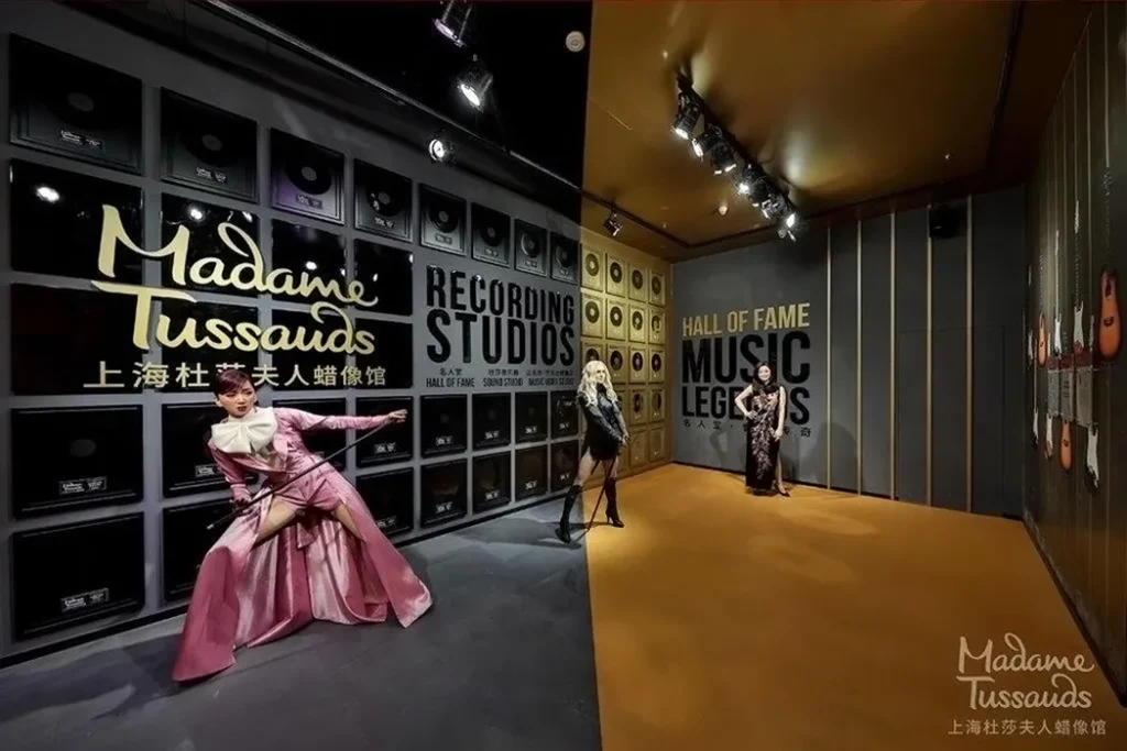 Madame Tussauds' Music Zone Hall of Fame corridor featuring life-sized wax figures of famous musicians, with a backdrop of wall-sized graphics resembling a recording studio and golden plaques.