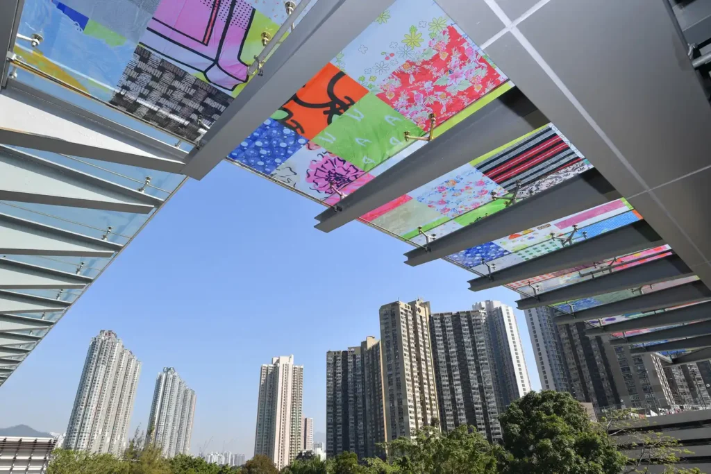 Colorful art installations on glass panels with urban high-rises in the background.