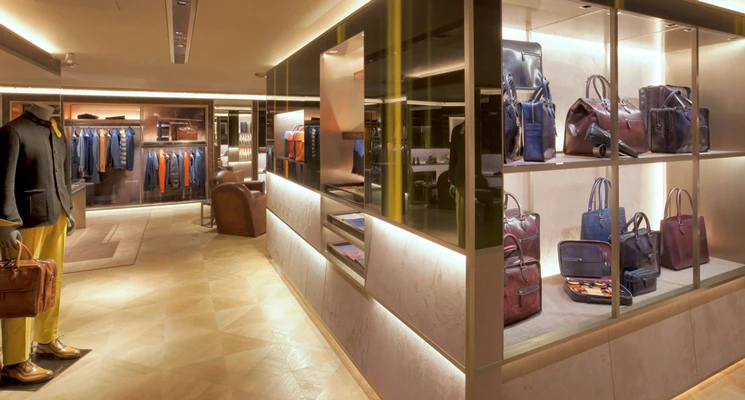 Interior of a men's clothing shop with racks of leather bags and garments, warm lighting, and a tiled floor.