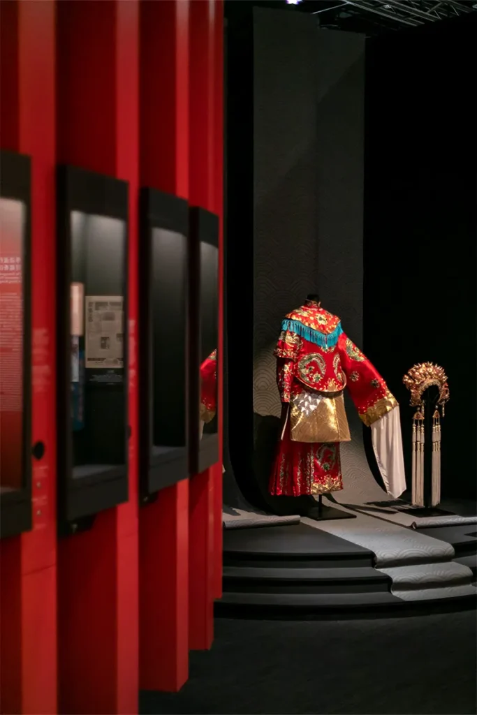 Red vertical frames lead to an intricate Chinese opera costume on display at the Hong Kong Heritage Museum highlighting the vibrancy of traditional Hong Kong arts.