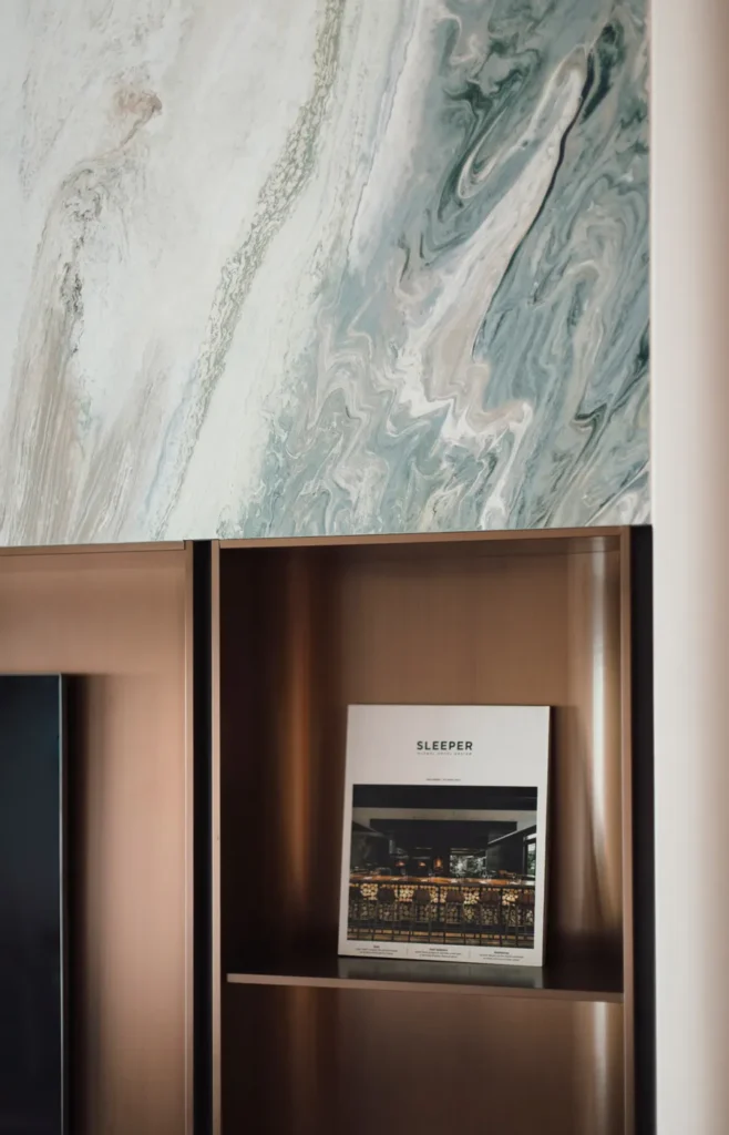 Close-up of a bespoke stone feature wall with a brass shelving unit designed by Rebel Arkitekt, highlighting the luxurious detailing and custom curation characteristic of a high-end residence.