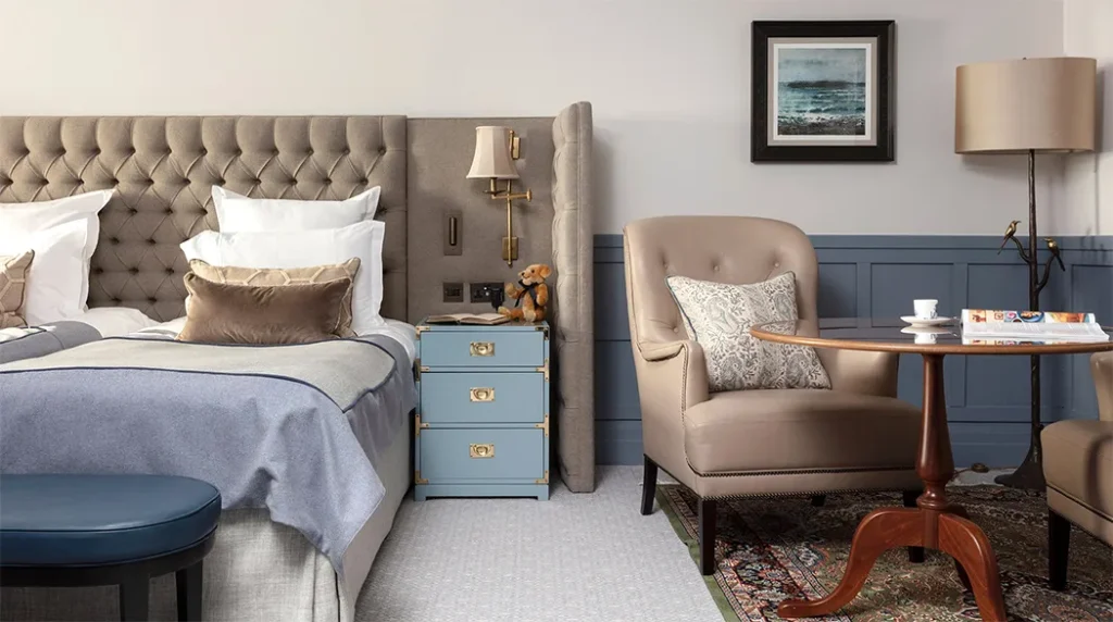 Cozy hotel bedroom with tufted headboard, elegant armchair, and soft lighting.