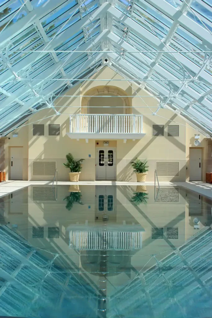 Indoor pool with transparent roof, reflections, and classical architecture details.