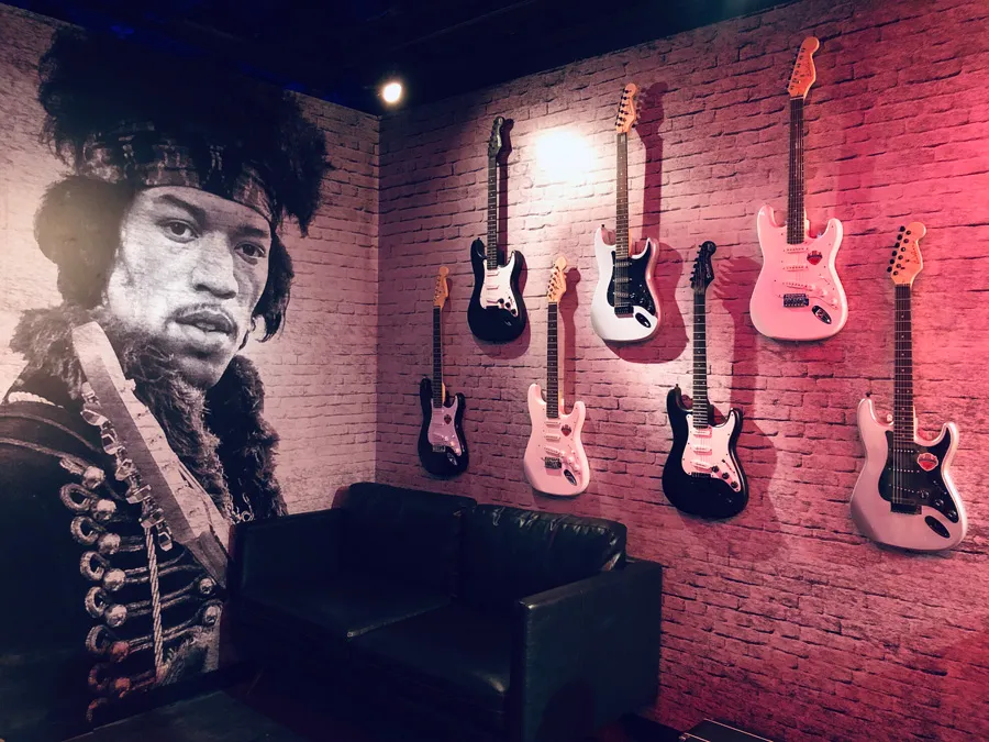 A mural of Jimi Hendrix and various models of guitars mounted on a brick wall in a studio setting.