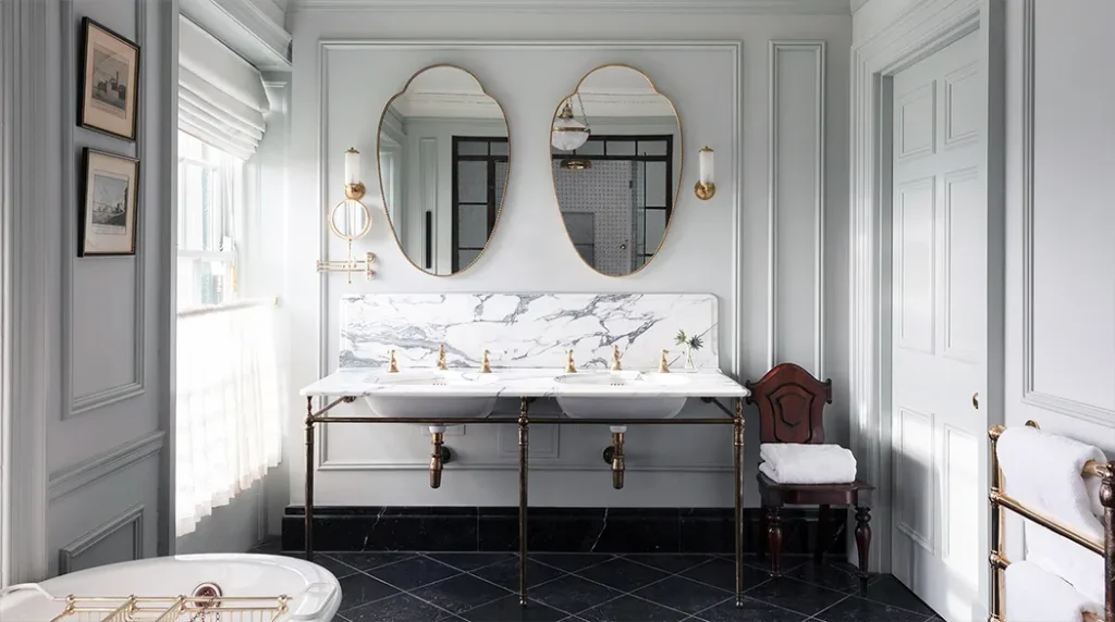 Luxurious bathroom with marble double sinks, gold fixtures, and oval mirrors.