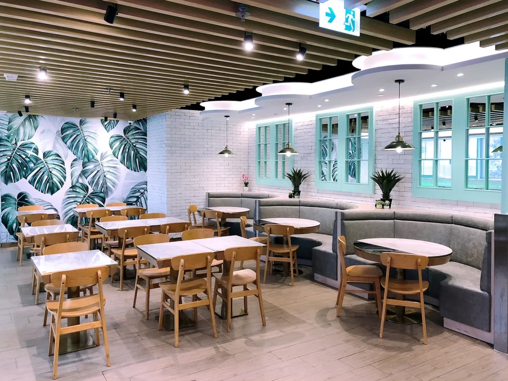 Lush botanical wallpaper accents the dining space with cozy booth seating and wooden tables, a design by Rebel Arkitekt enhancing M Kitchen's ambiance.