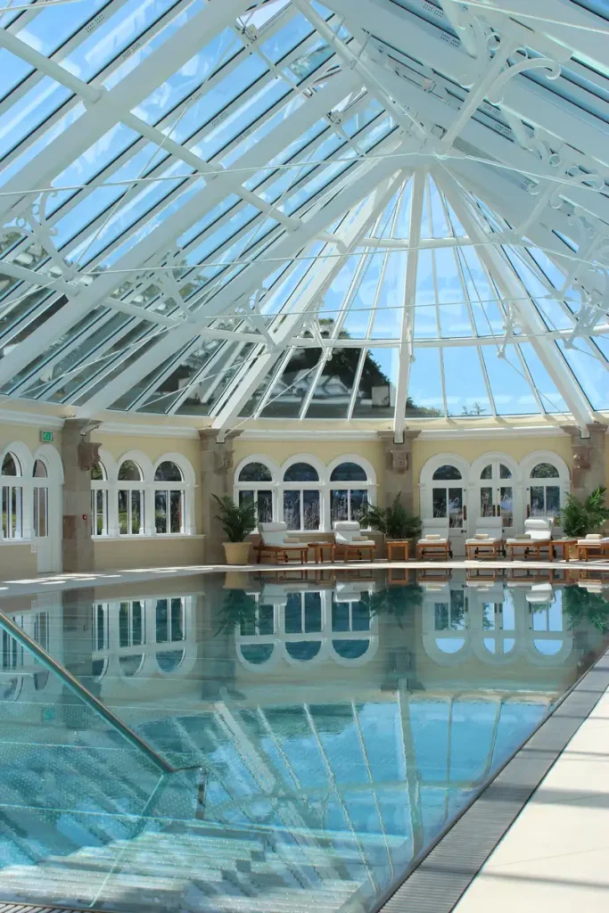 Sunlit indoor pool with arched windows and a transparent gabled ceiling.