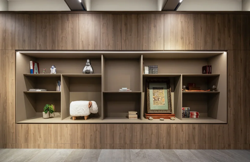 Sophisticated office bookshelf design by Rebel Arkitekt, highlighting a curated collection of objects on wooden shelves with integrated lighting, creating an inviting display area.