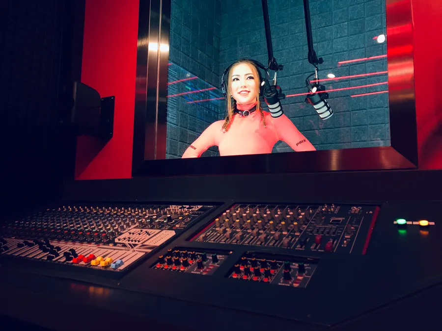 A recording studio's mixing console in the foreground with a vibrant red theme and a virtual image of a female artist singing in the background.