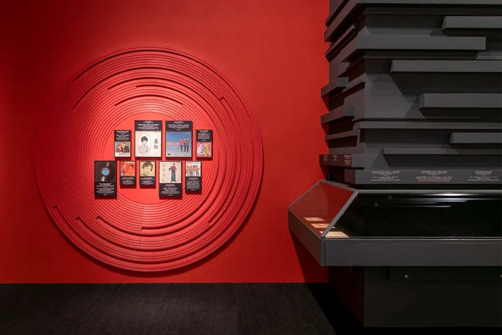 Project management by Rebel Arkitekt highlighted in the Hong Kong Heritage Museum with a striking red circular display wall featuring classic vinyl record covers, embodying the city's vibrant pop culture history.