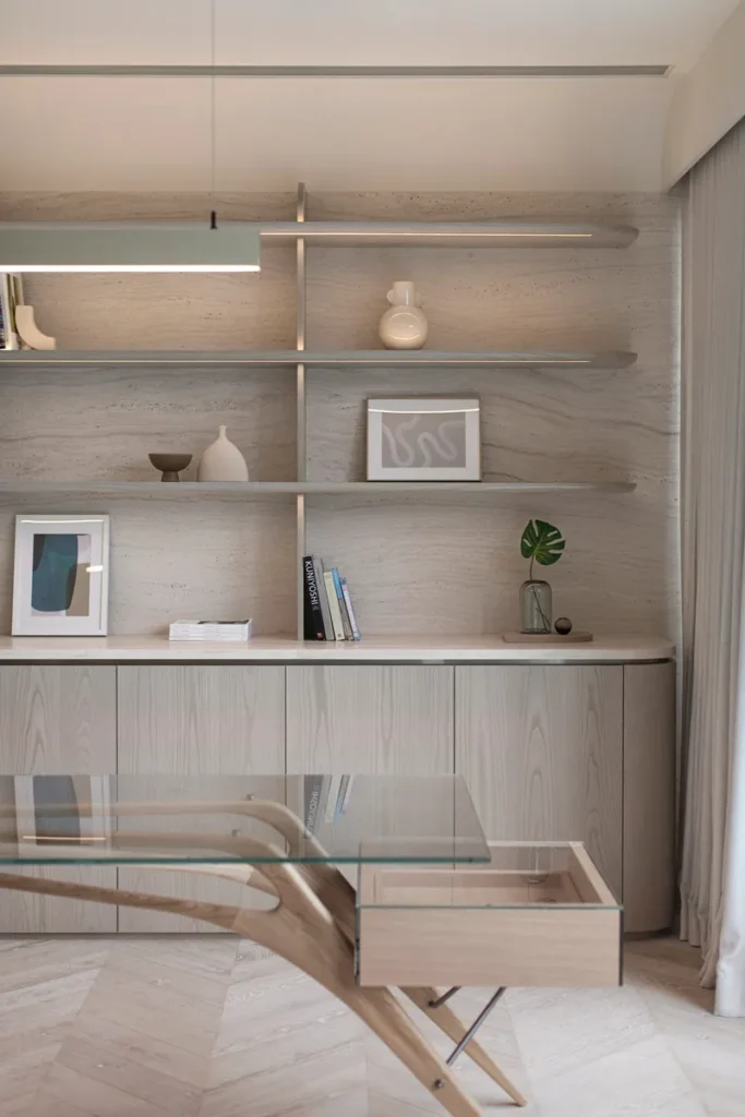 Contemporary study area boasting a sleek, glass-topped desk with wooden accents, complemented by floating shelves displaying minimalist decor against a textured wall.