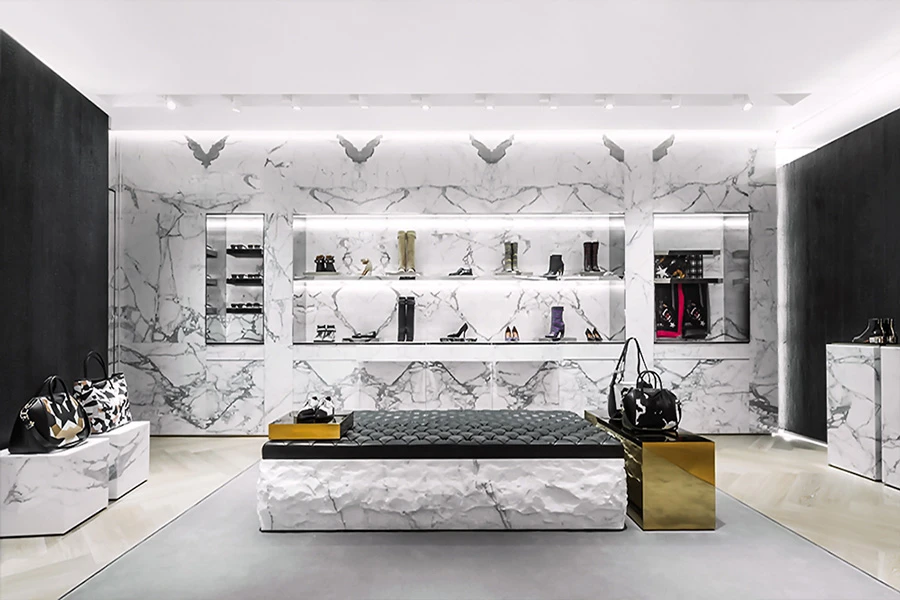 Luxury store interior with marble walls showcasing handbags on backlit shelves and central cushioned bench.