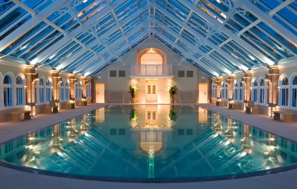 Twilight ambiance in a tranquil indoor pool with a striking glass ceiling and lit columns.