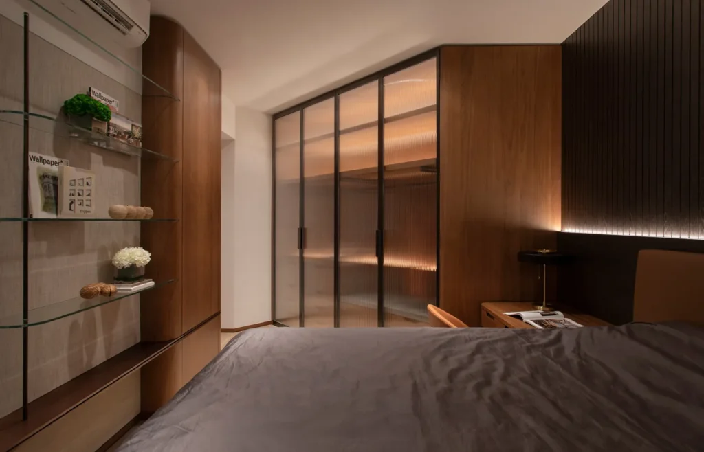 Warmly lit master bedroom designed by Rebel Arkitekt, featuring custom wood paneling, glass shelving with curated decor, and a translucent sliding door, all contributing to a serene and luxurious residential atmosphere.