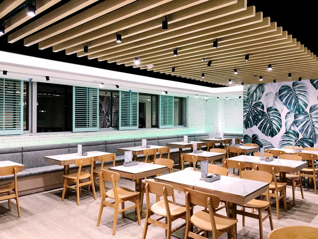 Chic and inviting M Kitchen dining area with grey booth seating, wood slat ceiling design, and tropical wallpaper, created by Rebel Arkitekt to capture the vibrant spirit of Hong Kong.