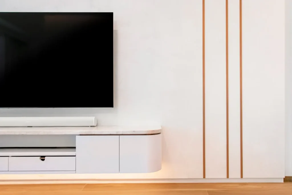 Sleek entertainment area with mounted flat-screen TV, custom-built white cabinetry with marble top, and vertical bronze inlays, designed by Rebel Arkitekt for a modern, minimalist home.