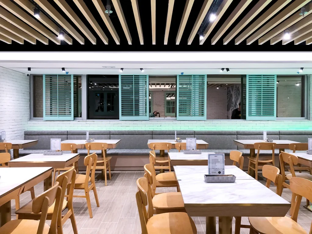 Streamlined dining space at M Kitchen with elegant marble tabletops and wood-accented ceiling, crafted by Rebel Arkitekt to reflect a serene yet modern atmosphere.