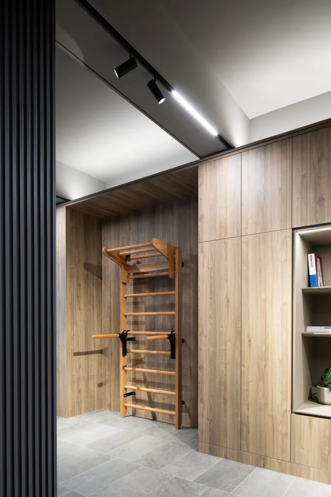 This Rebel Arkitekt-designed office incorporates wellness with a fitness area featuring a wall-mounted wooden pull-up bar, set against a backdrop of warm timber cabinetry, enhancing the space with both form and function.