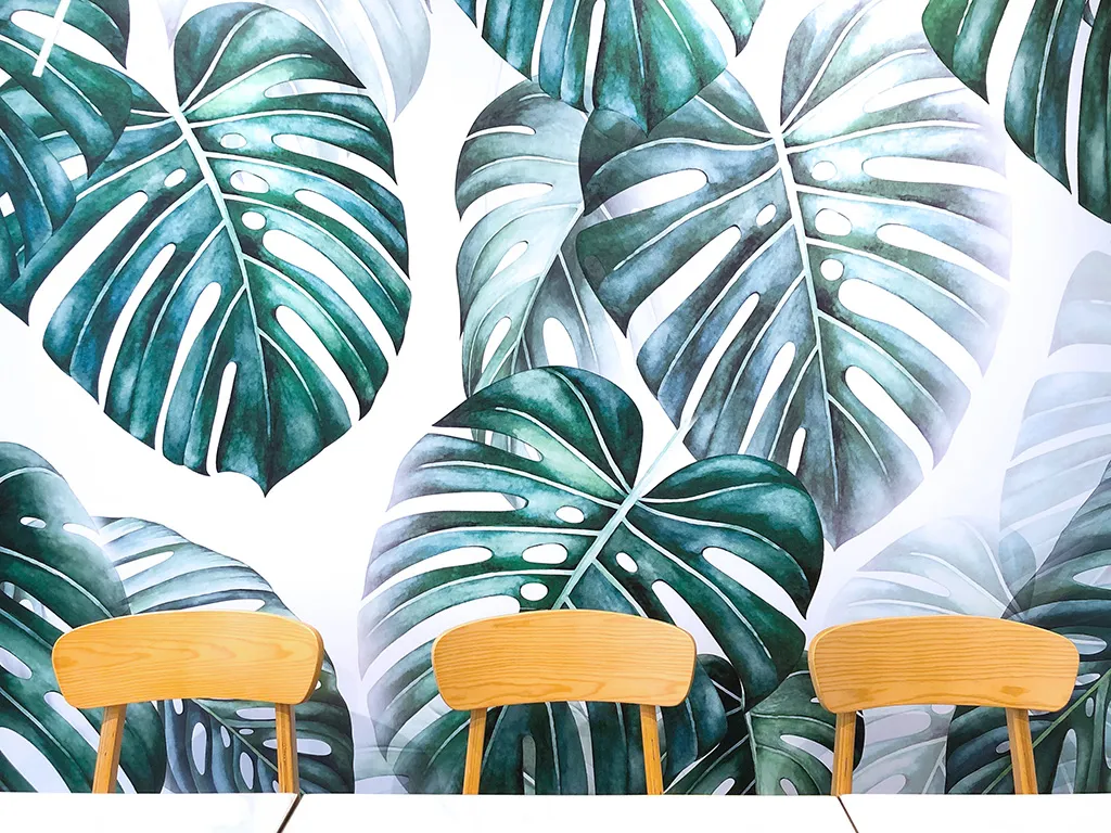 Artistic close-up of M Kitchen's dining chairs against a vibrant hand-painted monstera leaf mural, an accent piece curated by Rebel Arkitekt.