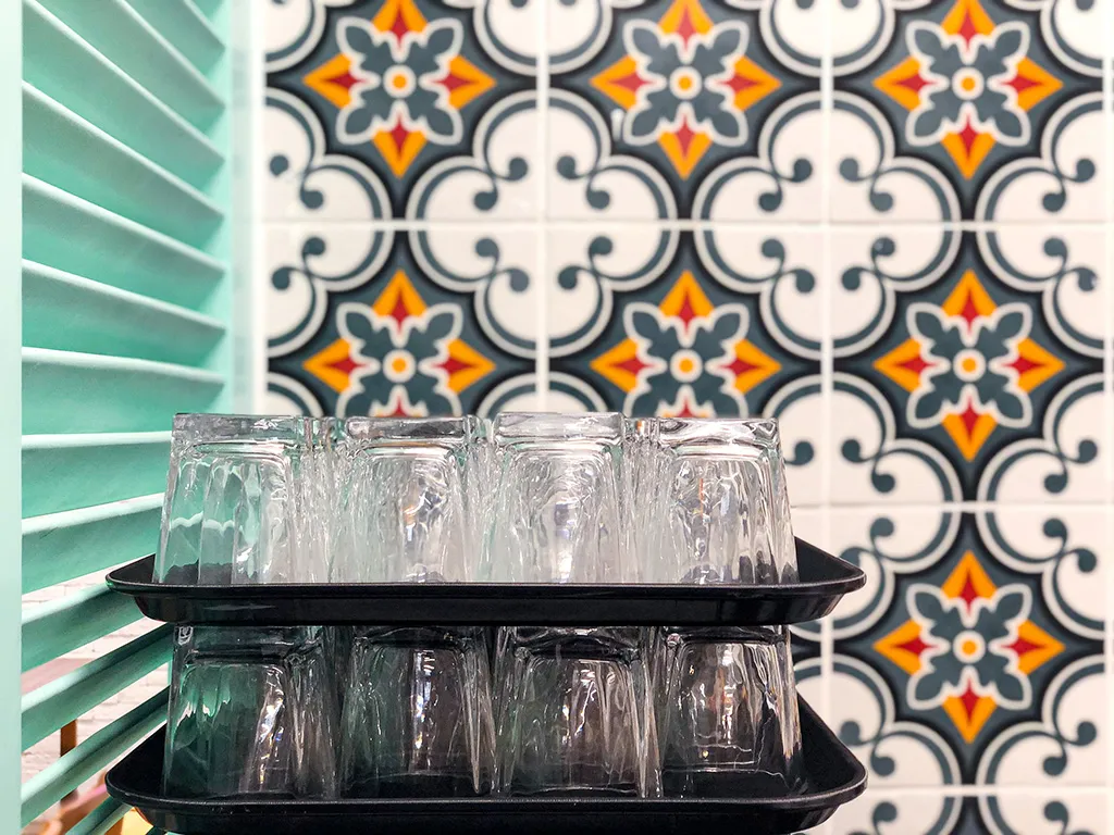 Detail of M Kitchen's ornate tile backsplash with traditional patterns beside modern mint green shutters, a contrast envisioned by Rebel Arkitekt.