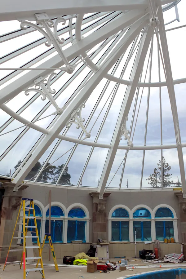 Indoor pool under construction with a striking skeletal glass roof and blue window covers.