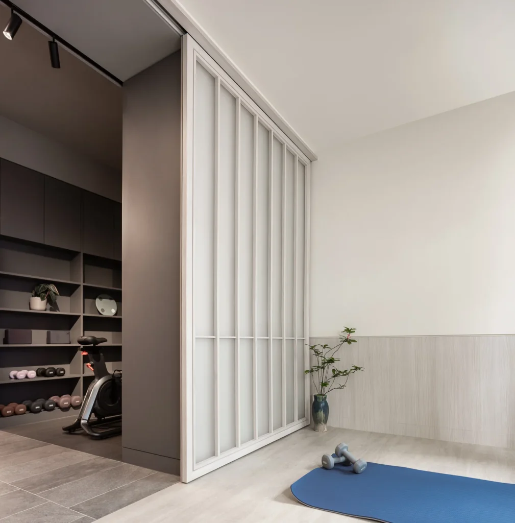 Translucent sliding doors crafted by Rebel Arkitekt open to a tranquil fitness area, where a yoga mat lies ready on the floor, hinting at mindfulness practices amidst the elegantly muted tones of the office design.