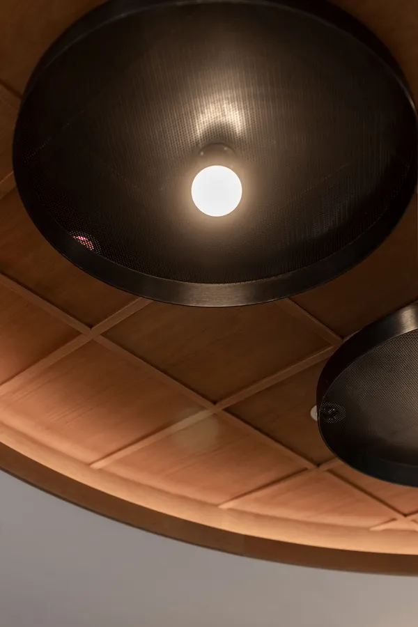 Elegant ceiling detail at DONDONYA x TORIKAI, showcasing black metal pendant lighting against a geometric wooden panel, a stylish design feature by Rebel Arkitekt.