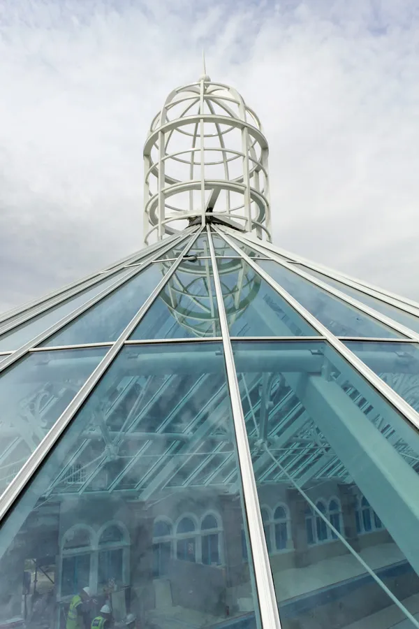 Geometric glass rooftop with metal frame and spherical structure against the sky.