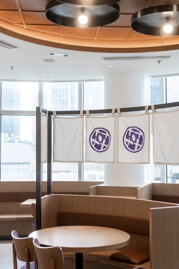 Cozy island booth seating at DONDONYA x TORIKAI under warm circular lighting, featuring distinctive branding banners, a thoughtful composition by Rebel Arkitekt.