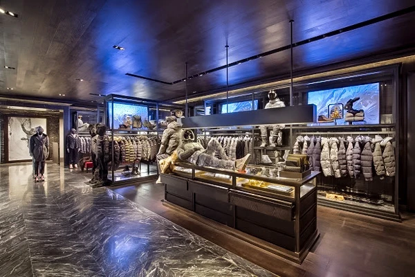 Interior of a ski clothing store with puffer jackets on display, dark wood decor, and marble flooring.