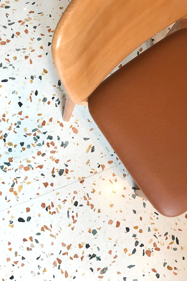 Detailed view of a brown leather chair against a playful terrazzo floor, juxtaposing textures in DONDONYA x TORIKAI's decor by Rebel Arkitekt.