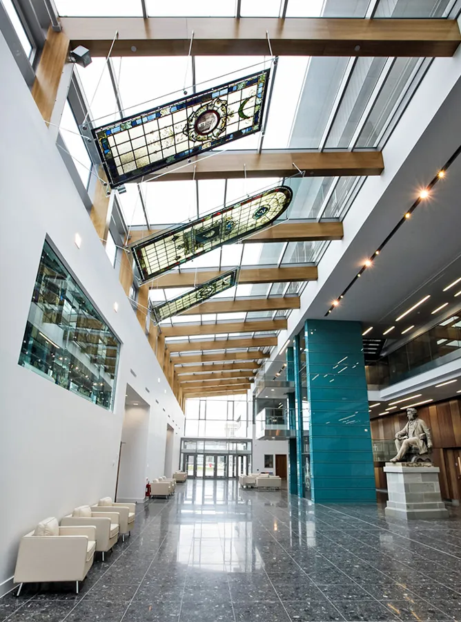 Modern veterinary school entrance with high ceilings, a glossy floor, wooden beams, and suspended stained-glass panels, accented by a statue for an educational feel.