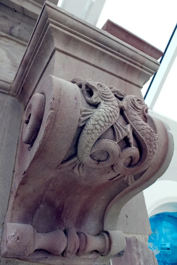 Intricate stone carving of entwined fish on a column at a poolside.