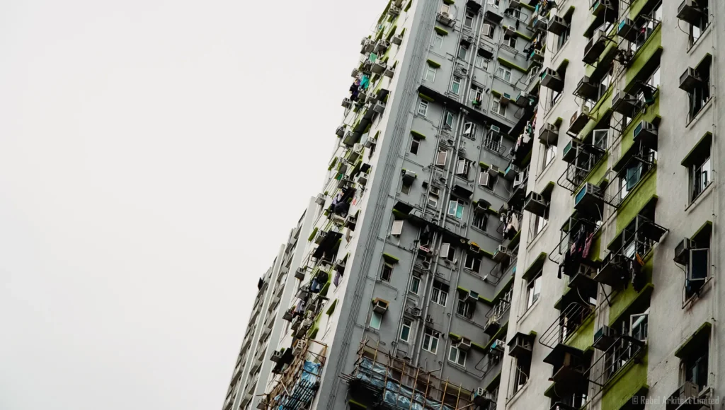 Dense urban fabric of Hong Kong in a photograph by Rebel-i, showing the textured façade of a residential building with a mosaic of windows and balconies.