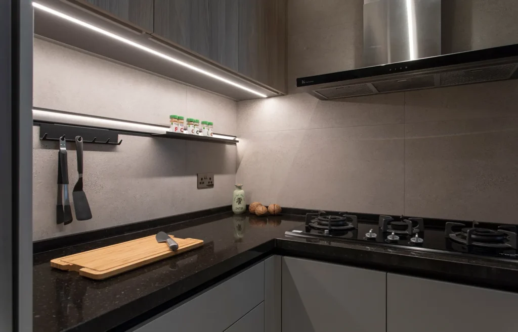 Functional and sophisticated kitchen design by Rebel Arkitekt, featuring under-cabinet lighting, a gas stove, and neatly arranged cooking essentials, with a focus on minimalism and practicality.