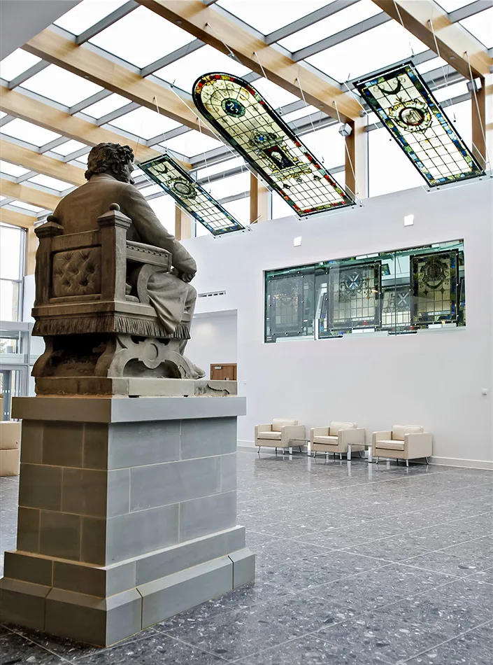 Modern veterinary school atrium with a polished granite floor, minimalist seating, and stained glass panels. A statue of founder William Dick presides in the naturally-lit space, showcasing a fusion of heritage and contemporary design.