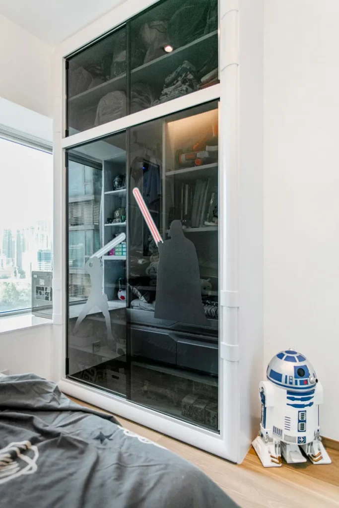 Star Wars insprired wardrobe with glass doors by Rebel Arkitekt, showcasing a collection of memorabilia, accompanied by a life-sized droid companion, creating a unique and playful atmosphere in the bedroom.