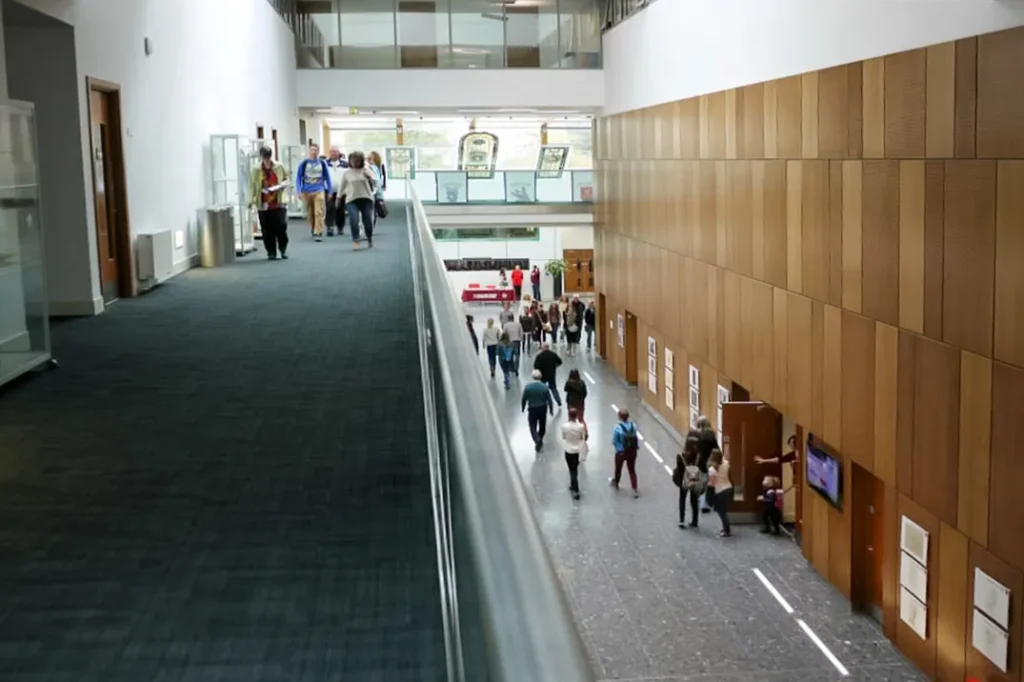 Spacious double-height atrium inside a veterinary school, featuring a library visible through large glass windows, modern seating areas, and a central staircase connecting the floors.