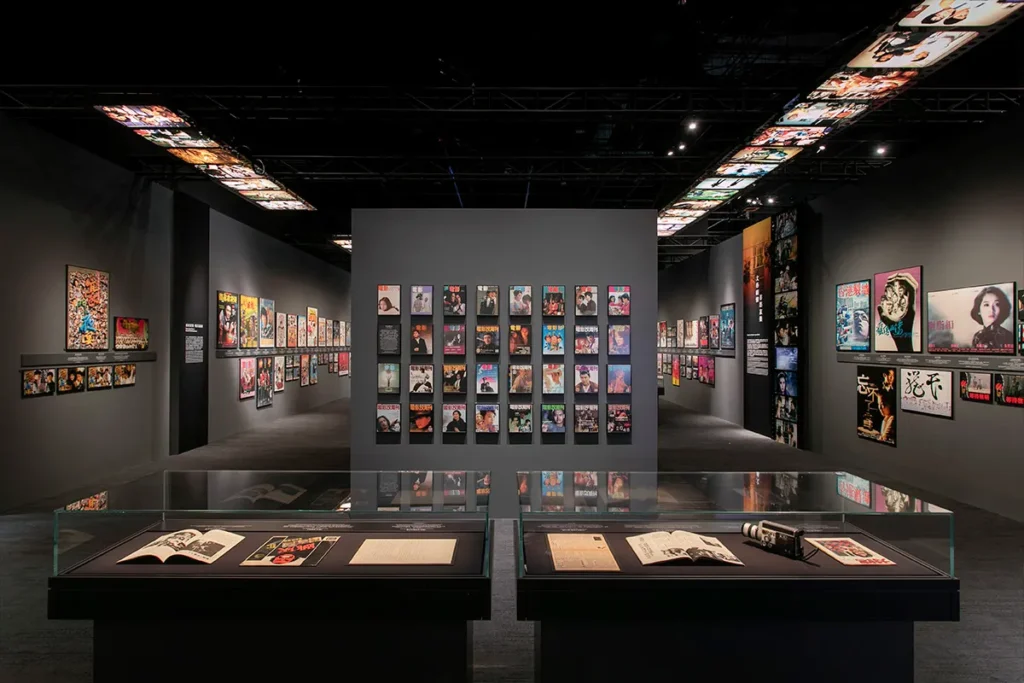 Interior of a gallery featuring an extensive collection of film memorabilia, with vibrant movie posters adorning the walls and vintage artifacts displayed in glass cases.