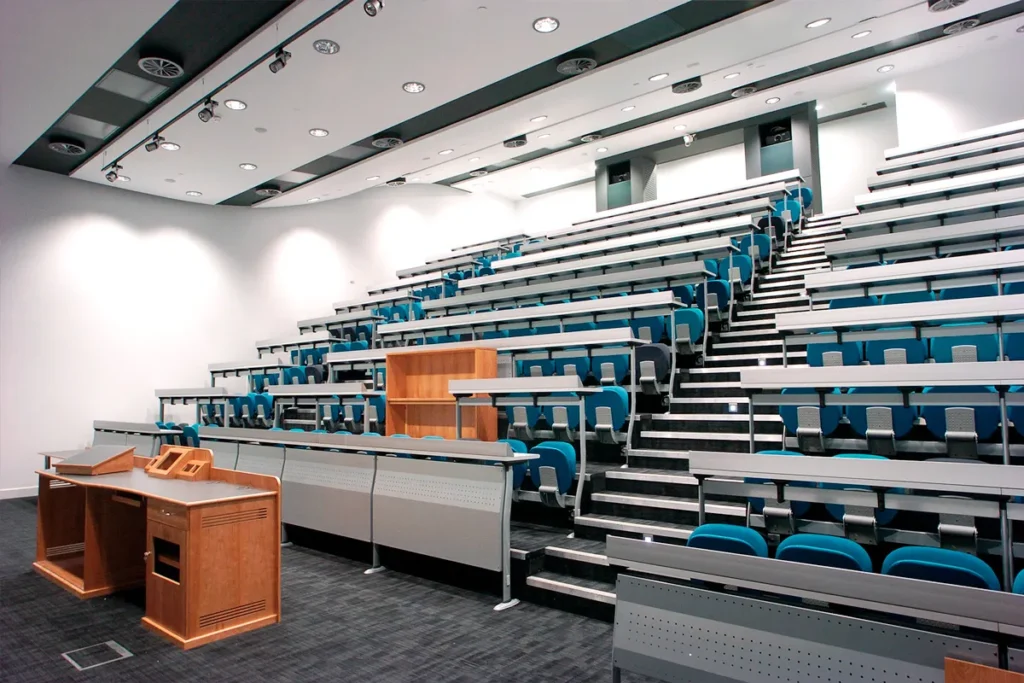 Modern empty university seminar room with staggered seating, blue chairs, and wooden podium.