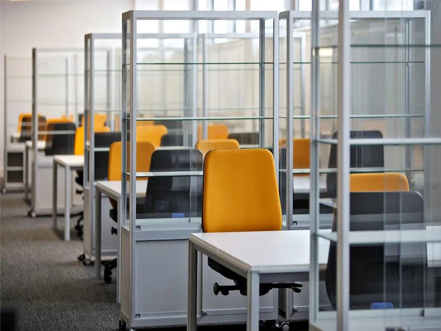 Study area with individual desks and yellow office chairs partitioned by transparent dividers in a brightly lit room.