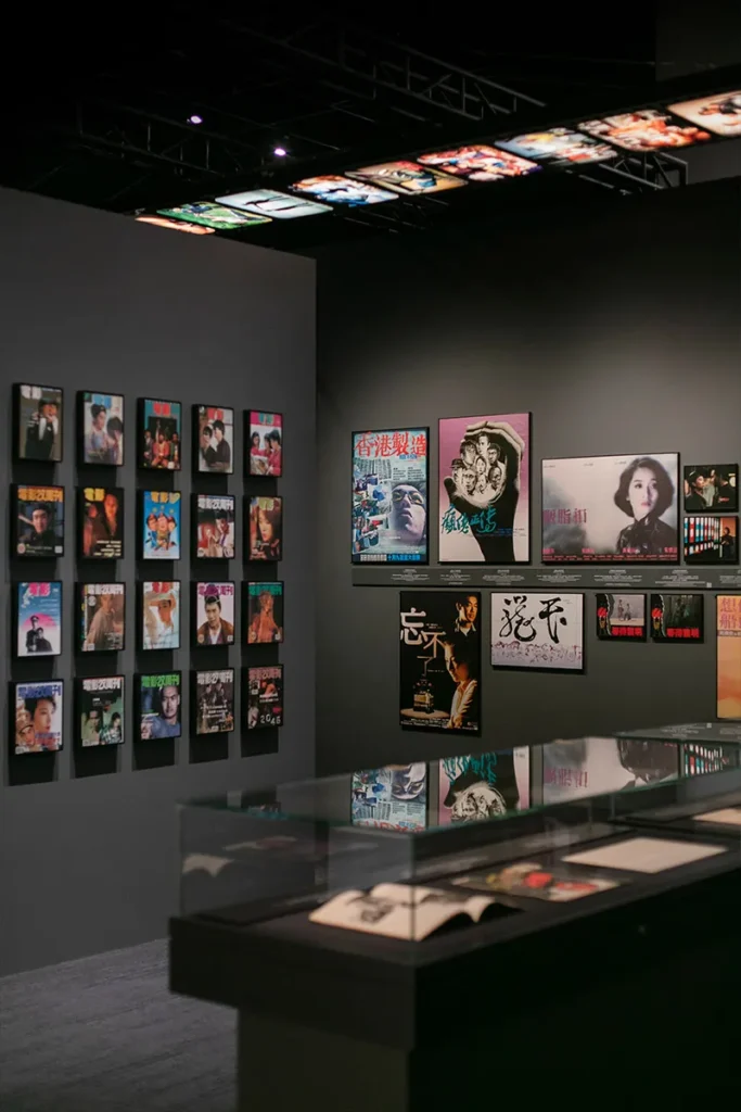 Museum wall displaying a collection of vintage and modern Asian film posters, with a reflective display case showcasing historical cinematic memorabilia.