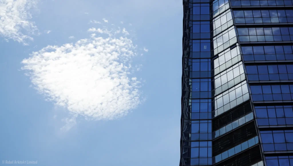 Contrast of architectural geometry and the organic form of clouds, a skyscraper's reflective glass façade artfully captured by Rebel-i under Rebel Arkitekt.