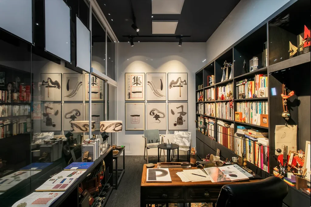 Intimate and reflective workspace display within a museum setting, featuring a classic wooden desk, chair, and various personal items, flanked by bookshelves filled with an extensive collection of books, awards, and cultural artifacts, symbolizing a personal journey through Hong Kong’s entertainment history and literary culture.